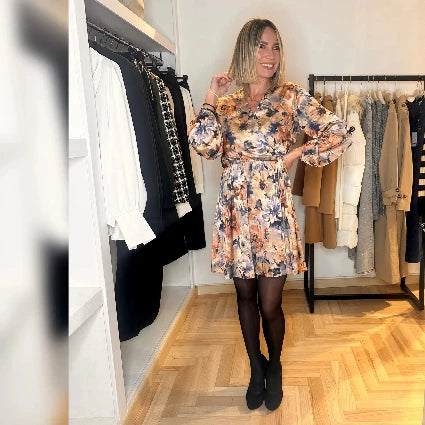 Una modella che indossa un abito corto con fiocco laterale e scollo a V in fantasia.