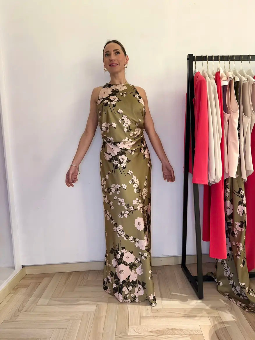 Abito lungo elegante Claset in raso verde oliva e fantasia a fiori con chiusura posteriore a due bottoni. Capo indossato da una sorridente modella presso la boutique a firenze