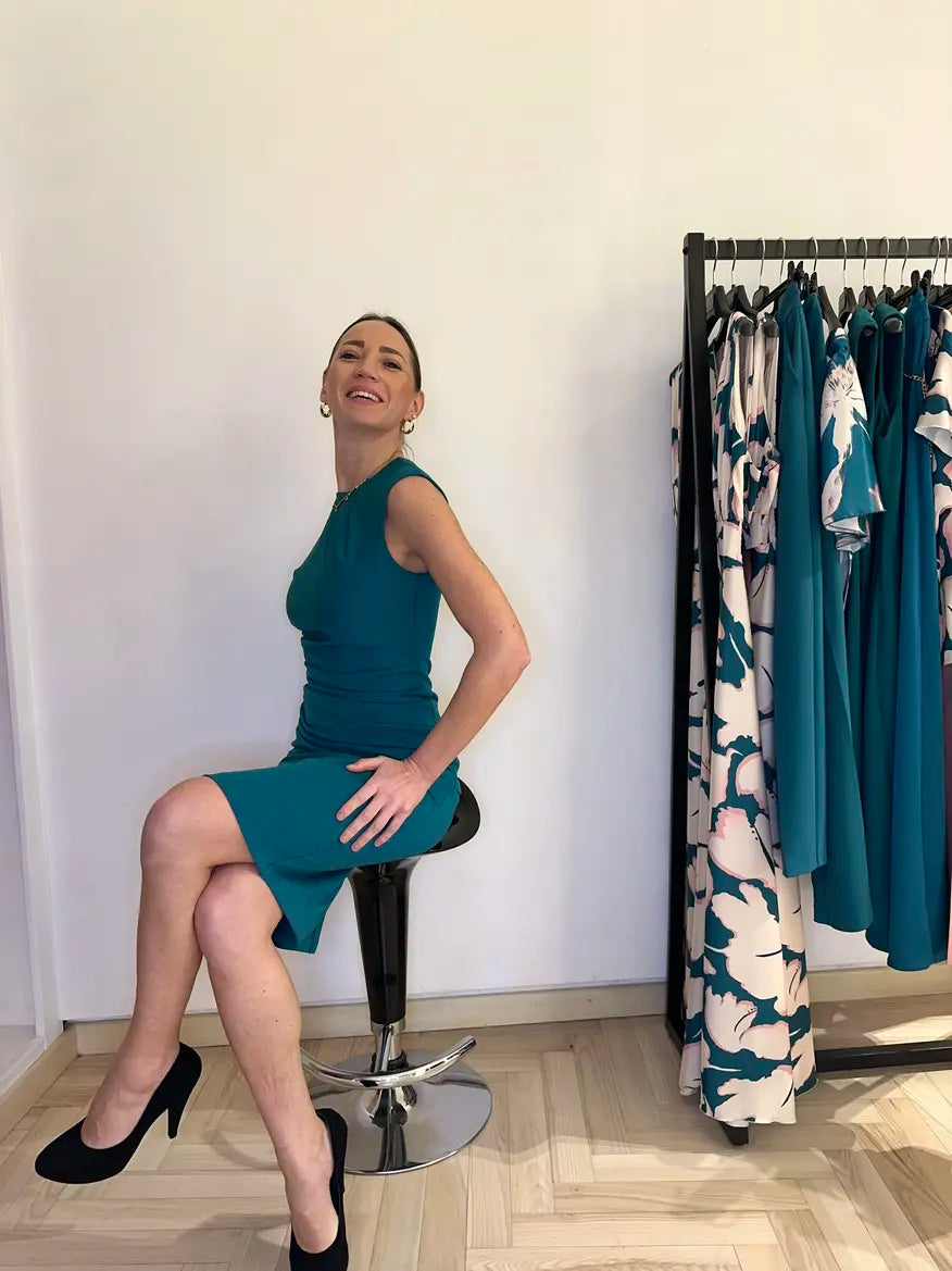 Abito verde smeraldo elegante Claset indossato da modella in boutique, taglio aderente con drappeggio laterale, stile raffinato per cerimonie o eventi