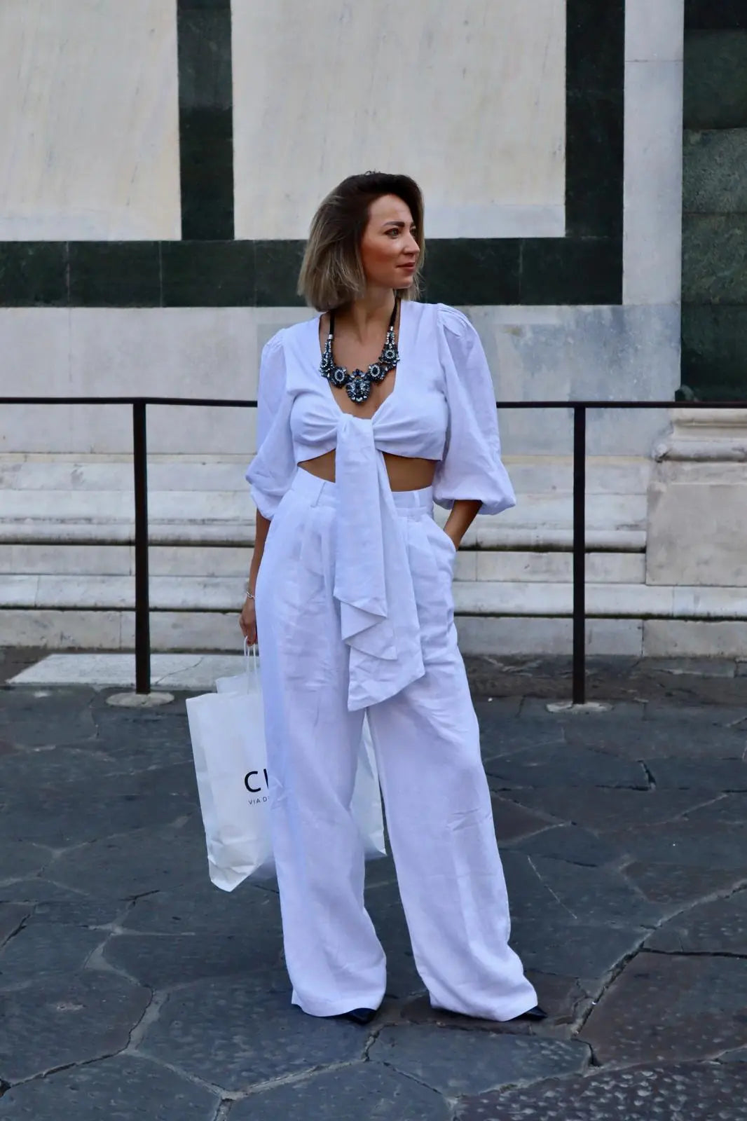 Bionda che indossa un pantalone a palazzo di lino bianco abbinato con il suo top a fiocco sulle strade di firenze