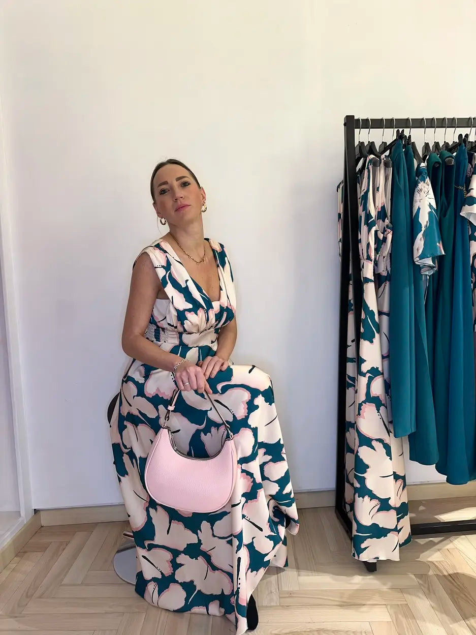 Abito lungo elegante Claset fantasia floreale beige e verde reale, con scollo a V e gonna ampia, indossato da modella con borsa rosa cipria in boutique