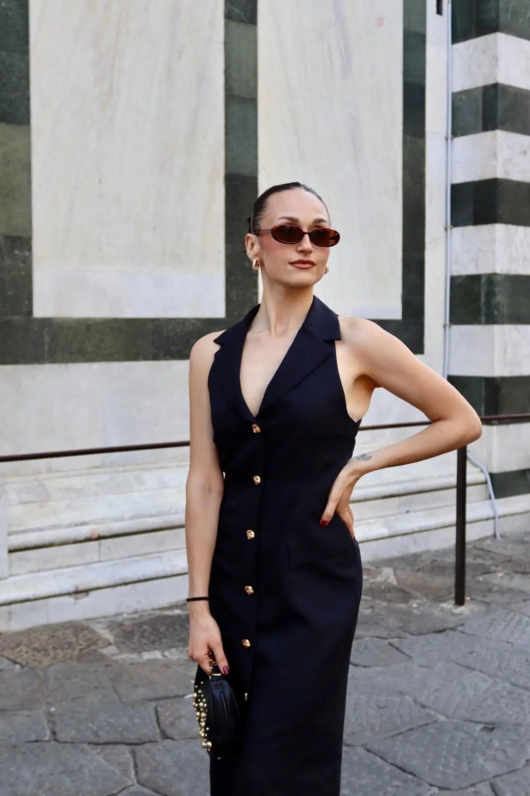 modella che indossa un abito midi nero con dettagli bottoni oro frontali. Un capo perfetto per un aperitivo tra amiche o una cena fuori d'estate a Firenze