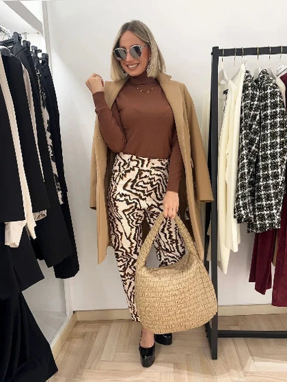 Foto con modella bionda con occhiali  da sole che indossa un outfit casual autunnale beige molto confortevole con  jeans e dolcevita e un cappotto con borsa trapuntata